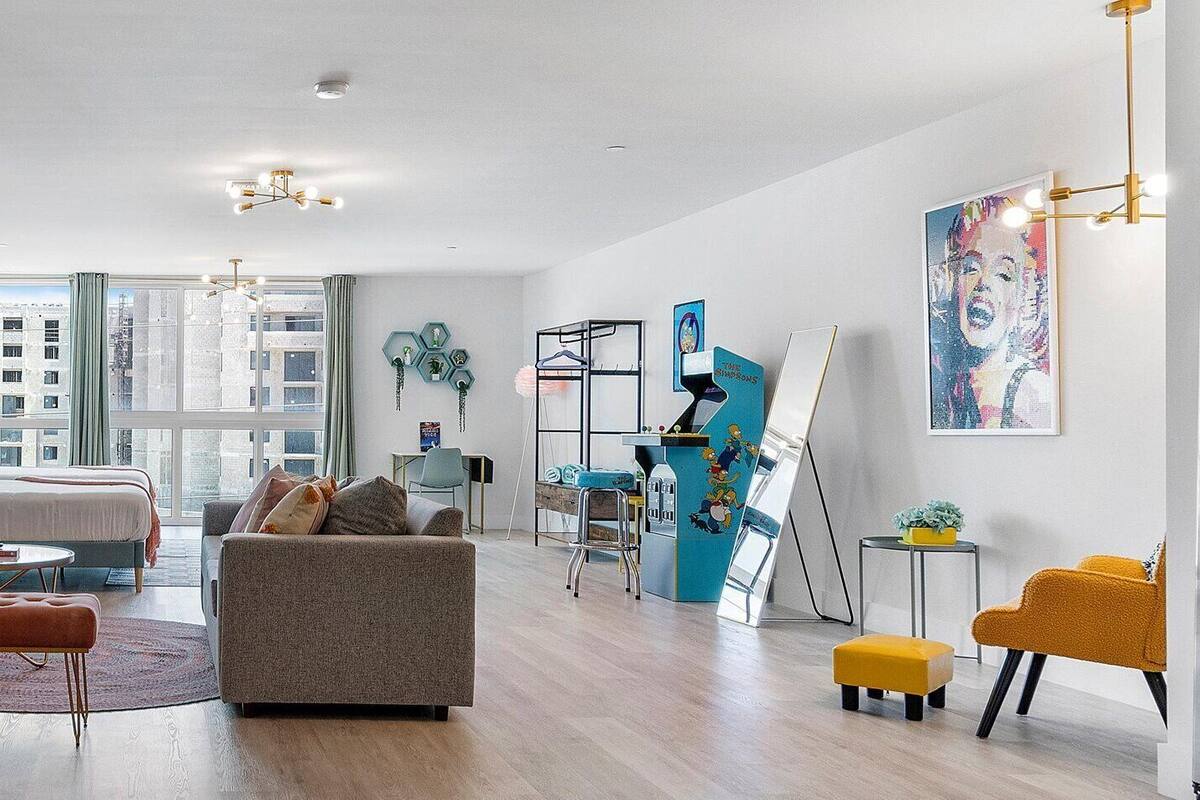 A modern living room with a dining area, a sofa, a coffee table, and a TV. There are framed pictures on the wall and a window with a view of buildings.