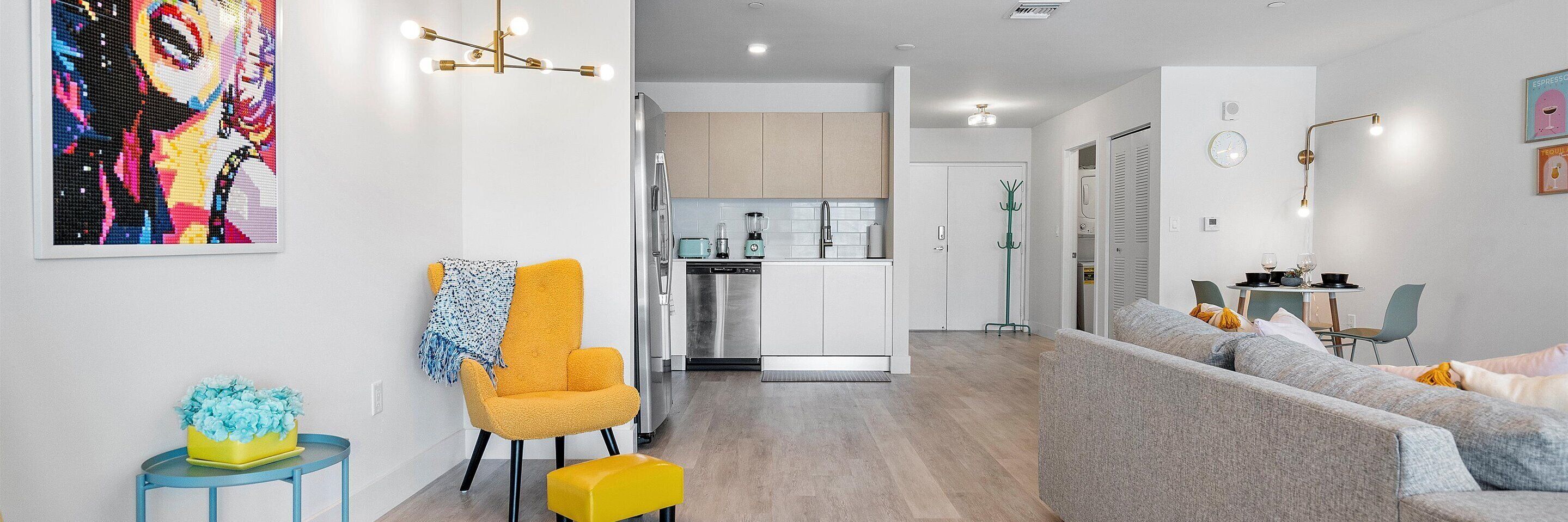 A modern living room with a sofa, a yellow armchair, and a small table with a blue vase.