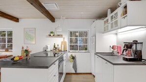 Eine moderne Küche mit weißen Schränken, einer schwarzen Arbeitsplatte und einem Fenster mit Blick auf Bäume. Auf der Arbeitsfläche steht eine Kaffeemaschine und ein Wasserkocher.