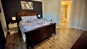 Ein Schlafzimmer mit einem hölzernen Bett, einem Nachttisch mit Lampe, einem Deckenventilator und einer Tür zu einem anderen Raum.