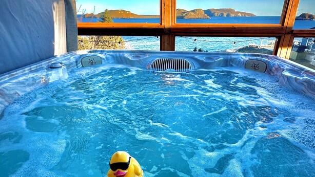 Ein Whirlpool mit einem quietschenden Gummientchen mit Sonnenbrille, umgeben von einer Holzterrasse und einem malerischen Meerblick.