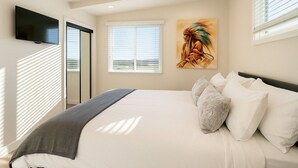 Un dormitorio con una cama grande, un televisor de pantalla plana montado en la pared y una ventana con persianas.
