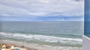 A view of the ocean from a balcony with a beach and a building in the foreground.