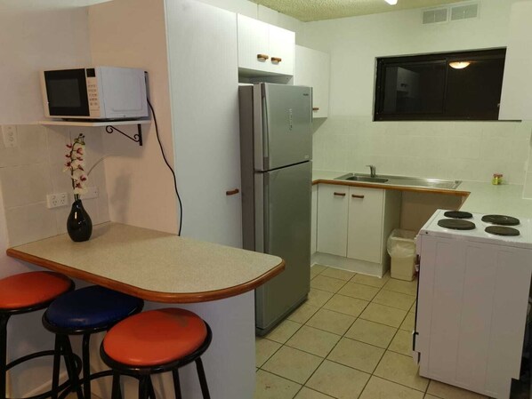 A compact kitchen with a refrigerator, microwave, and stove. There are three stools and a small sink.