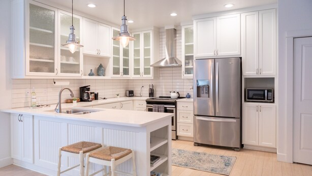 A modern kitchen with white cabinetry, stainless steel appliances, and a central island with stools. - Centrally Located (Eugene)