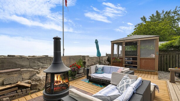 A wooden deck with a stone wall, a fire pit, outdoor furniture, and a small wooden structure.