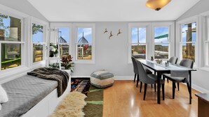 A modern dining area with a long table, chairs, and a bench. There are large windows with views of the outside.