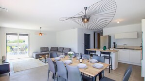 A modern dining area with a wooden table set for six, grey upholstered sofas, and a kitchen with white cabinets and a black countertop. - Awesome home in Cléon d'Andran (Cléon d'Andran)
