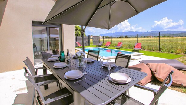 An outdoor dining area with a table set for two, a pool, and lounge chairs in the background. - Awesome home in Cléon d'Andran (Cléon d'Andran)