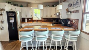 Una cocina con armarios blancos, un refrigerador negro y una isla de madera con taburetes de bar.