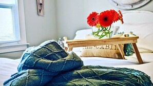 Una cama bien hecha con una manta azul, una pequeña bandeja de madera con flores, y una almohada con la etiqueta "THE CABIN".
