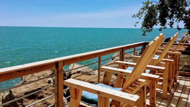 Una terraza de madera con sillones de descanso frente a una costa rocosa y el océano.