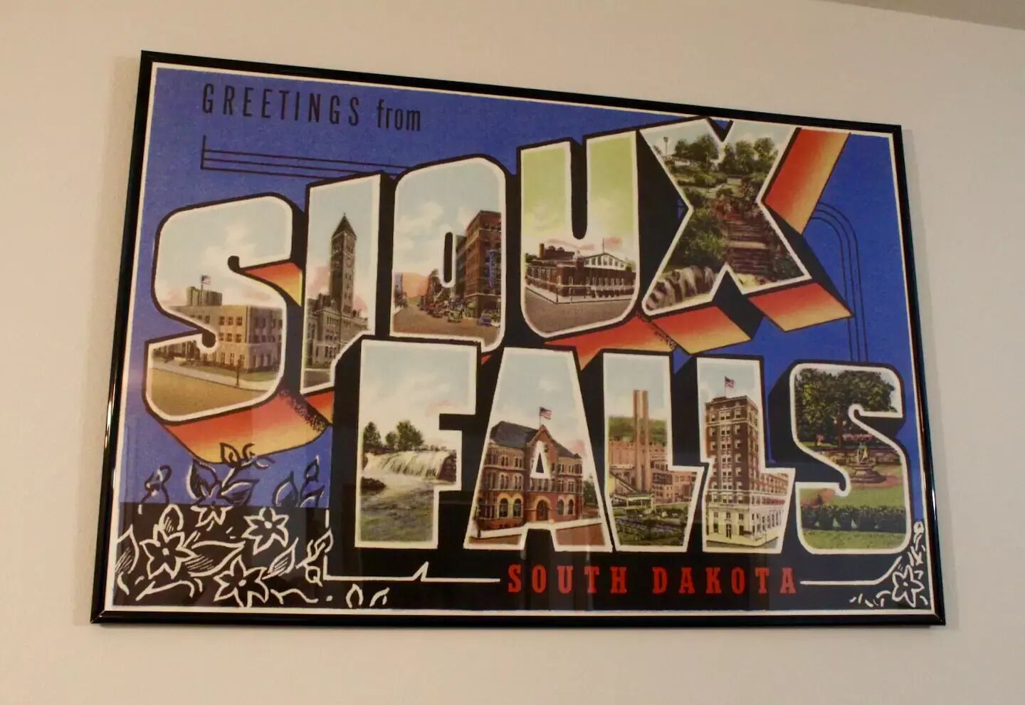 Cartolina incorniciata con la scritta “Greetings from Sioux Falls, South Dakota” e diverse immagini di edifici e monumenti.