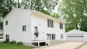 A two-story white mobile home with a front porch, a garage, and a small front yard. - Downtown Apartment Perfect for Short & Extended Stays (Sioux Falls)