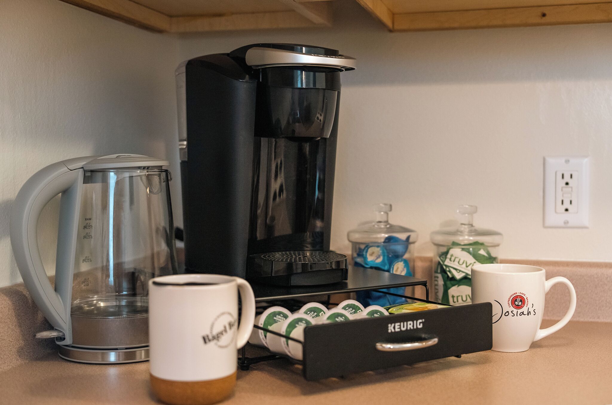 Una cafetera, una taza, un portacápsulas de café y una jarra de leche sobre una encimera de cocina.