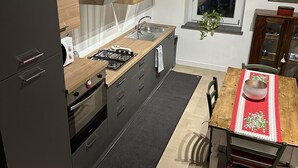 Et moderne køkken med mørke skabe, en træbordplade og et spiseområde med et træbord og stole.