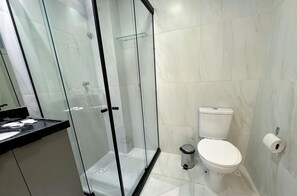 A modern bathroom with a glass shower enclosure, a toilet, and a sink with a black countertop. - Paradise Beach (João Pessoa)