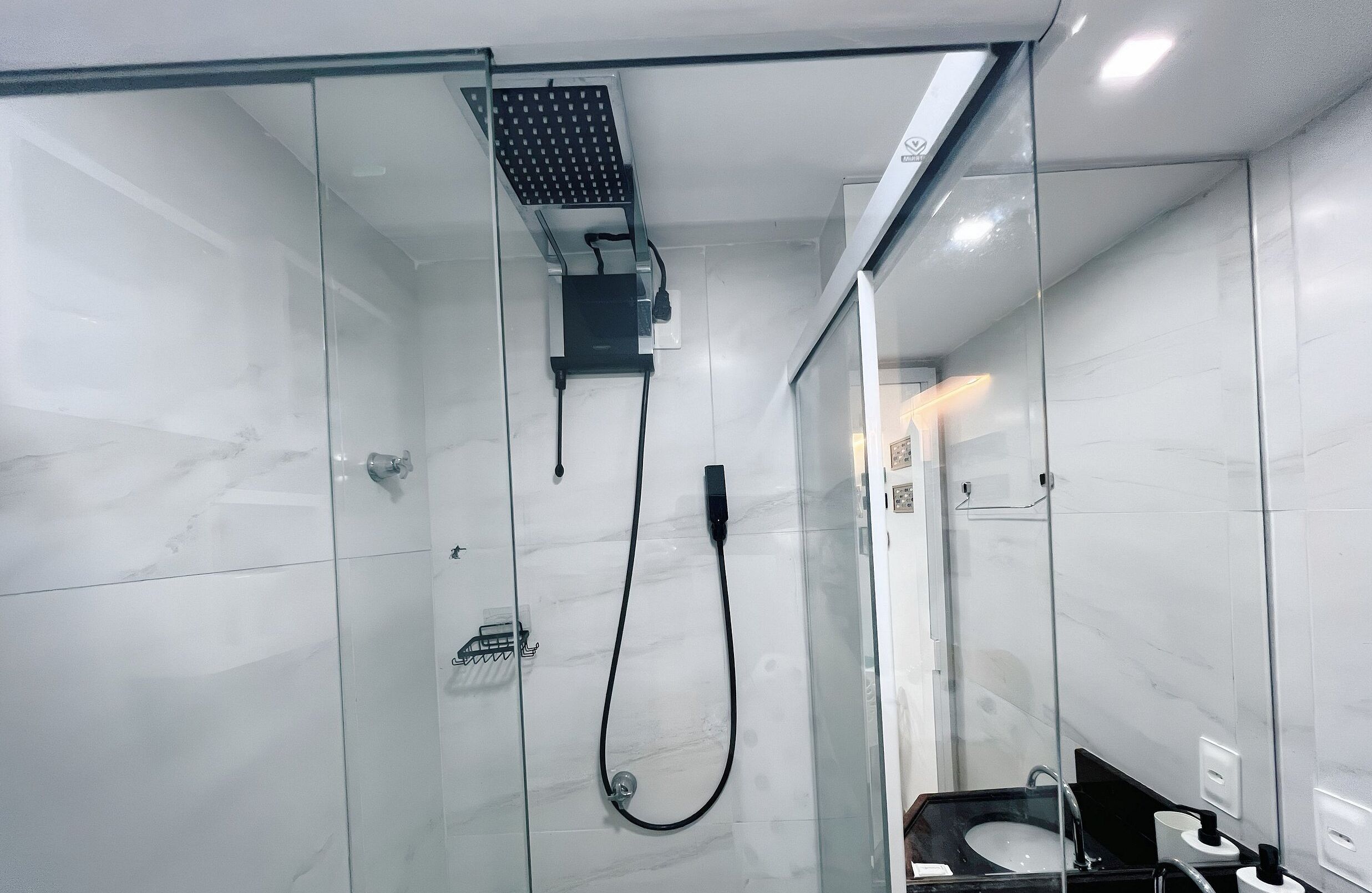 A modern bathroom with a glass-enclosed shower, a black sink, and a white marble wall.