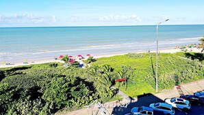 A beach with parked cars, umbrellas, and greenery. - Paradise Beach (João Pessoa)