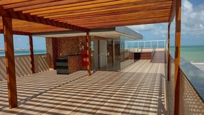 A covered outdoor area with a checkered floor, a glass wall, and a view of the sea. - Paradise Beach (João Pessoa)