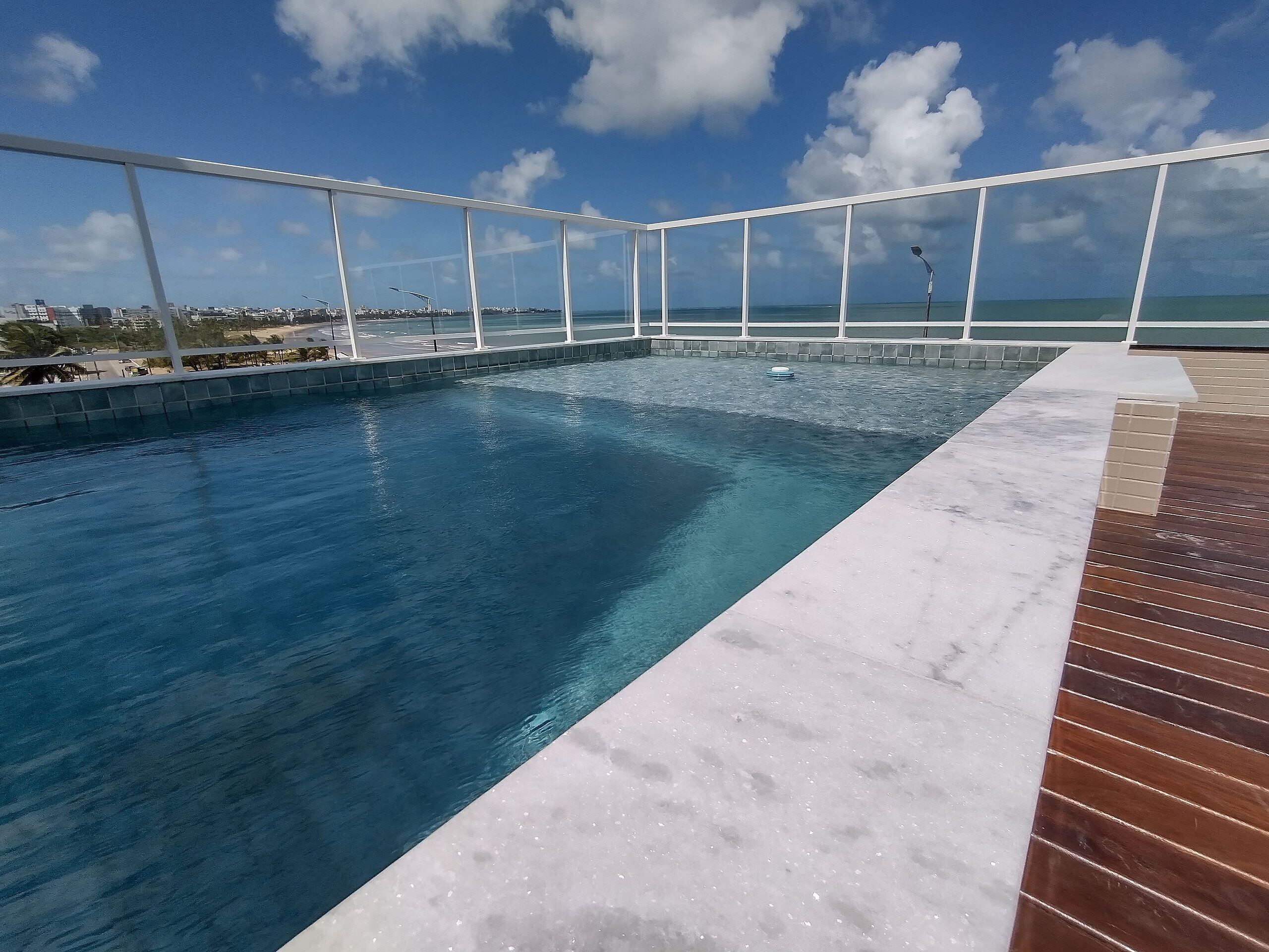 Una piscina con cubierta de madera y barandilla de vidrio.