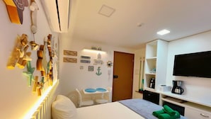 A hotel room with a bed, a desk with two chairs, a TV, a coffee maker, and wall decorations including a sign that says "BEACH". - Paradise Beach (João Pessoa)