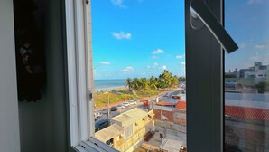 A view from a window overlooking a coastal area with buildings, palm trees, and a clear sky. - Paradise Beach (João Pessoa)
