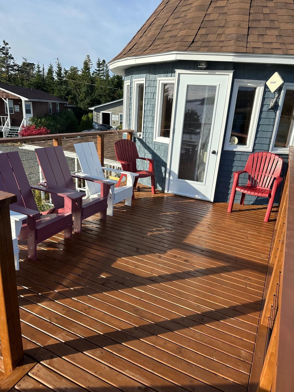 Um deck de madeira com cadeiras Adirondack e uma porta de vidro que dá para um edifício com fachada azul.