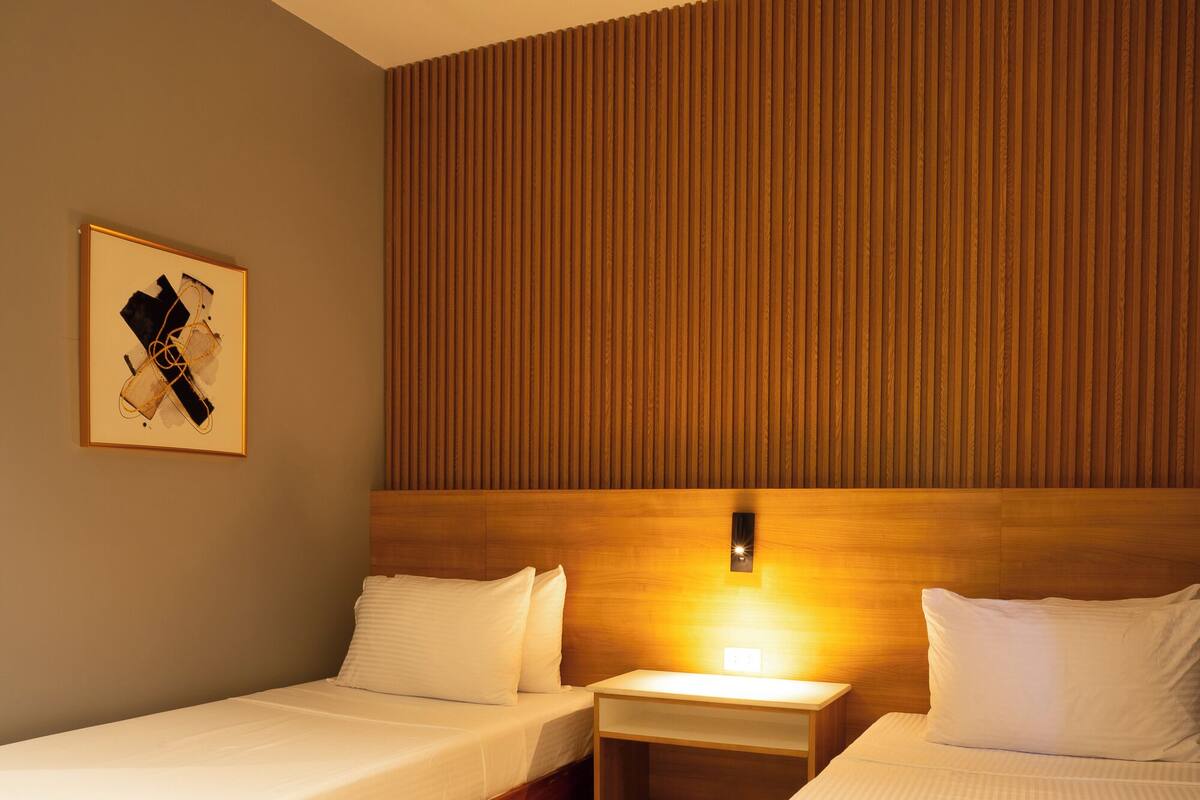 Een hotelkamer met twee houten bedden, een nachtkastje met een lamp en een lijst met een foto aan de muur.