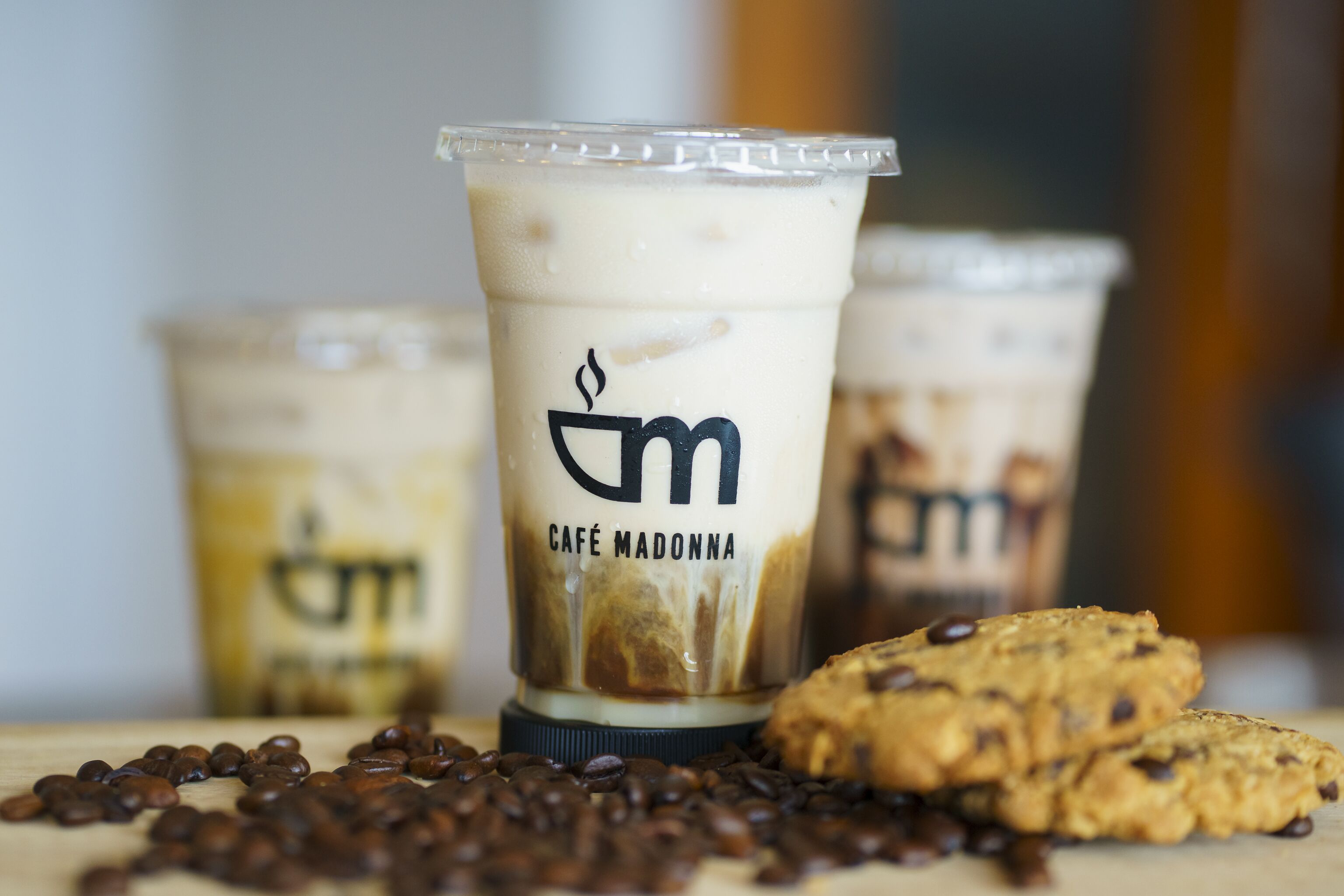 Een close-up van een beker met het opschrift 'Café Madonna' en een koekje ernaast.