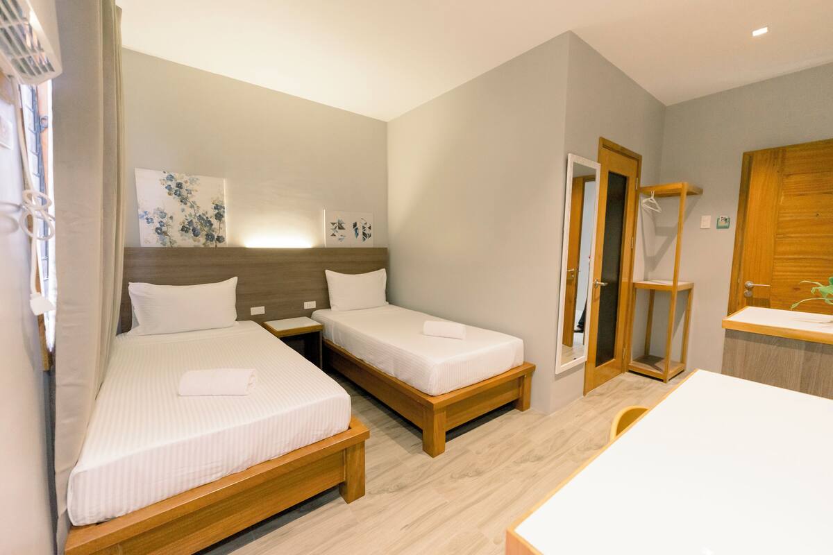 Een hotelkamer met twee enkele bedden, een houten hoofdbord, een nachtkastje, een klein bureau en een stoel.