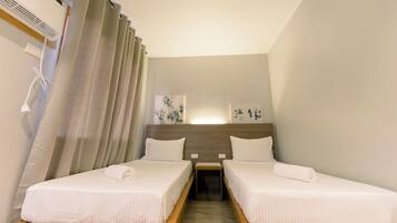 A hotel room with two single beds, a wooden nightstand, a wall-mounted air conditioner, and a curtain.