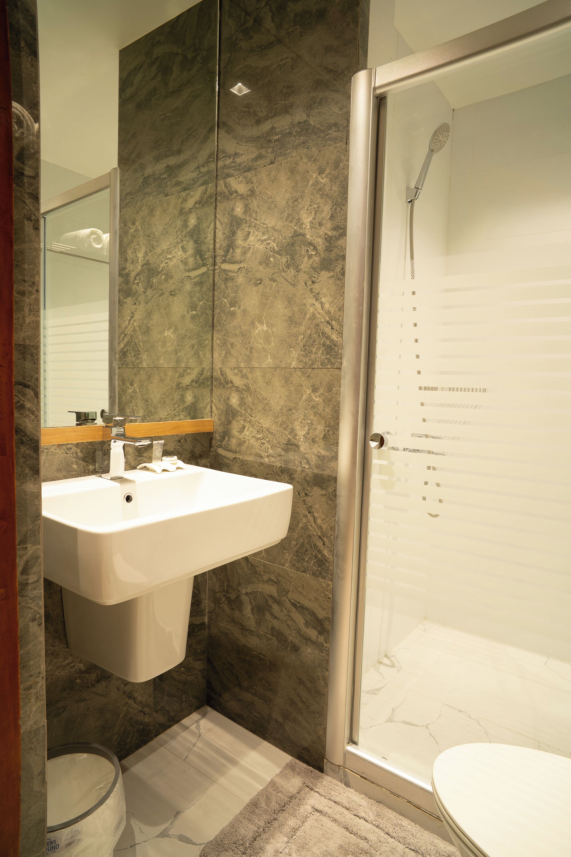Un baño con lavamanos de mármol, cabina de ducha de cristal y retrete.