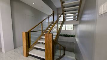 Una escalera moderna con barandillas de madera y paneles de vidrio, que conduce a un segundo piso con vistas a espacios verdes al exterior.