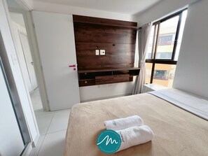 A hotel room with a bed, a wooden wall unit, a window with curtains, and a door. - Urbani Smart Residence (João Pessoa)