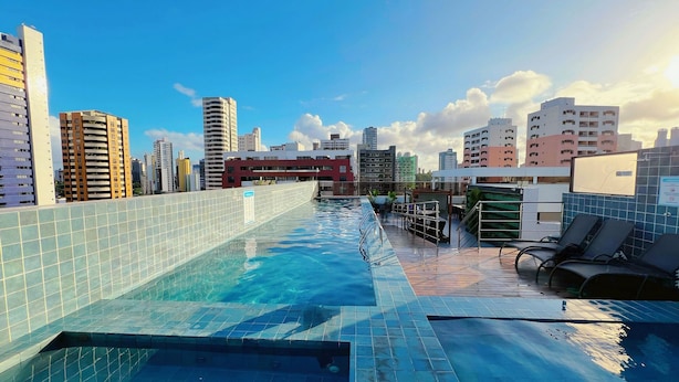 A rooftop swimming pool with a cityscape view, surrounded by buildings and a clear sky. - Urbani Smart Residence (João Pessoa)