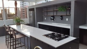A modern kitchen with a central island, bar stools, a gas stove, and a built-in refrigerator. - Urbani Smart Residence (João Pessoa)