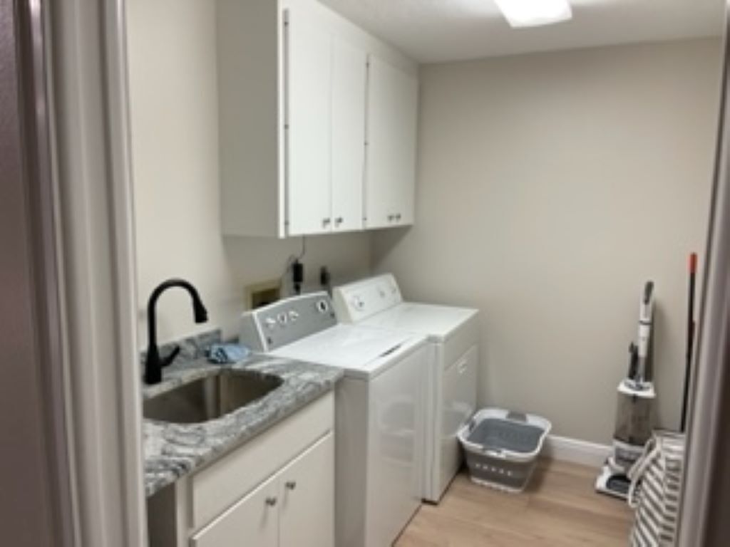 Un espace buanderie comprenant un lave-linge, un sèche-linge, un évier et un aspirateur.