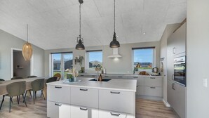 Una cocina moderna con una isla central, iluminación colgante y grandes ventanales que ofrecen vistas al exterior.