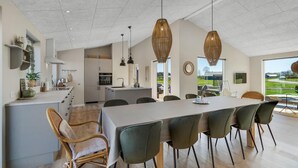 Una cocina amplia con electrodomésticos modernos, un comedor con una mesa grande y sillas, y vistas al exterior a través de un ventanal.