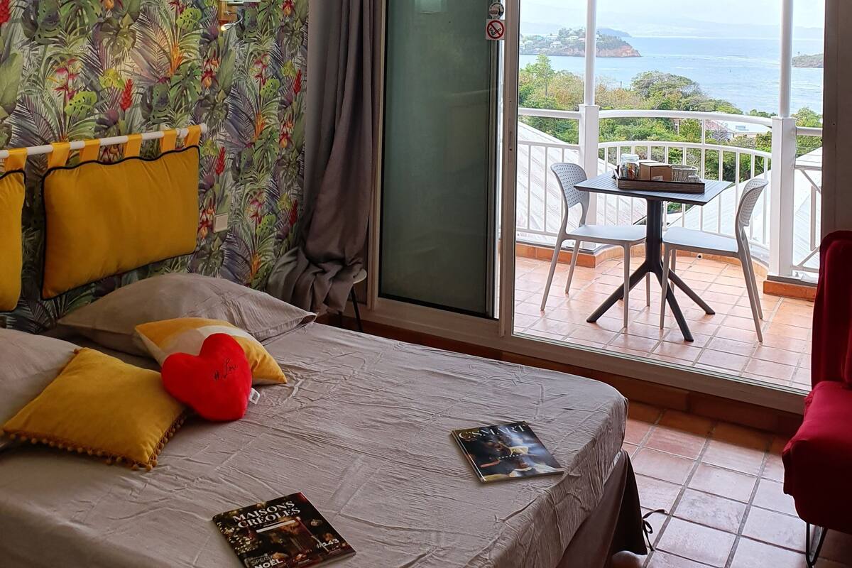 Une chambre avec un lit, une table de chevet, une fenêtre donnant sur la mer et un balcon avec une table et des chaises.