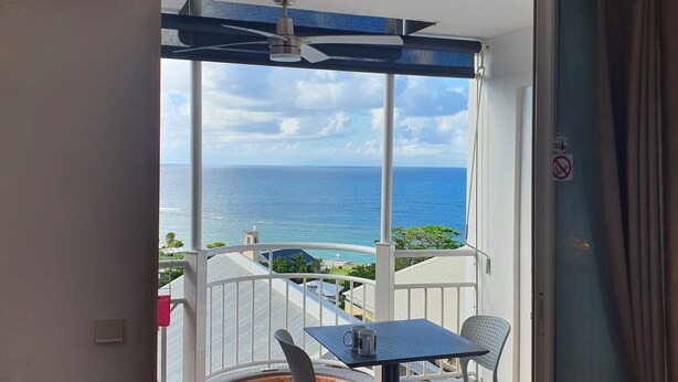 A balcony with a table and chairs, a ceiling fan, and a view of the ocean. - Studio abricot 309 (La Trinité)