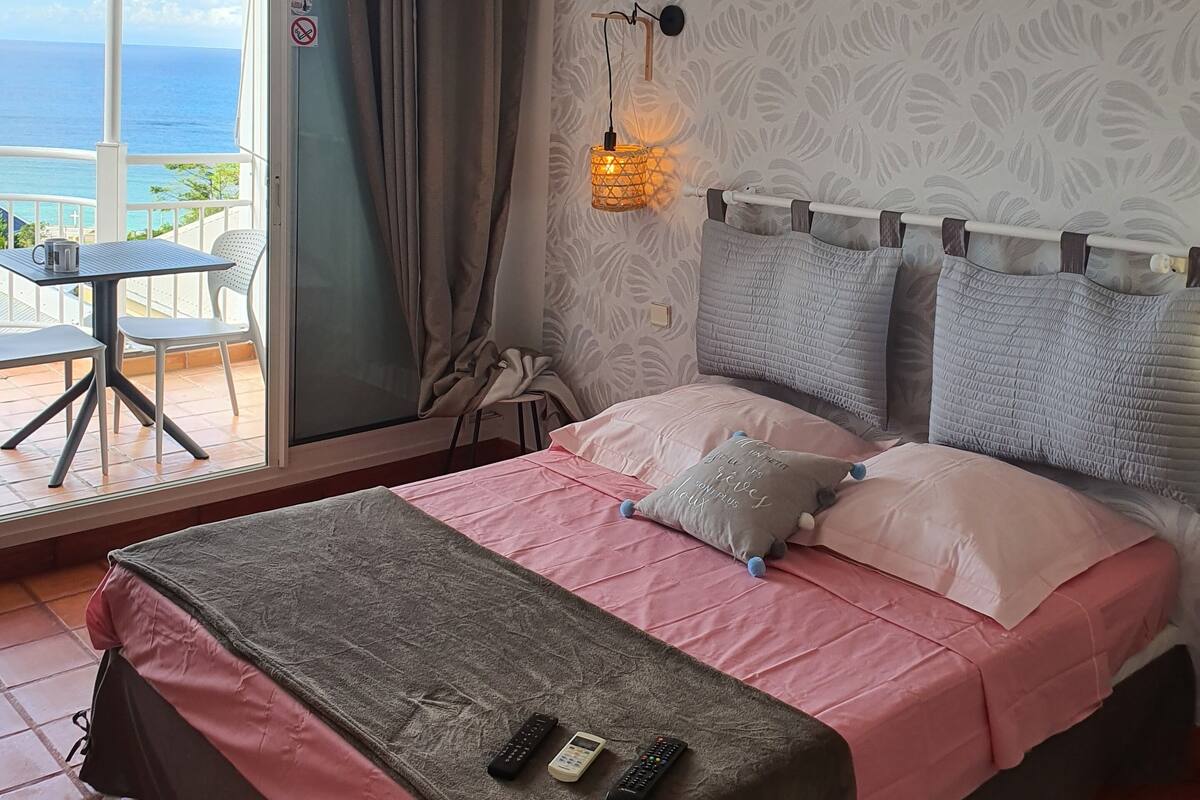 Une chambre avec un lit, une table, des chaises, une vue sur l’océan et un mur décoré de motifs.