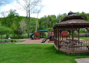 Relax in a shaded gazebo surrounded by a playground and lush greenery.