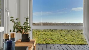 Une vue depuis une fenêtre donnant sur une terrasse en bois, avec une plante en pot et une bougie sur une table.