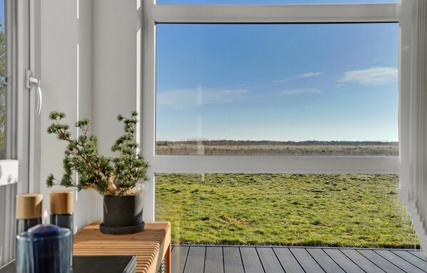 Blick aus einem Fenster mit Holzterrasse, Blumentopf und Kerze auf einem Tisch.