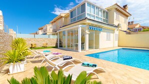 Ein modernes Haus mit Schwimmbad, Liegestühlen und einer Steinmauer.
