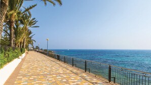 Eine Küstenpromenade mit einem gemusterten Gehweg, Palmen und freiem Blick auf das Meer.