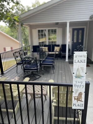 Ein überdachter Außenbereich mit Tischen und Stühlen, ein Schild mit der Aufschrift "The Lake is my Happy Place" und im Hintergrund ein Haus.