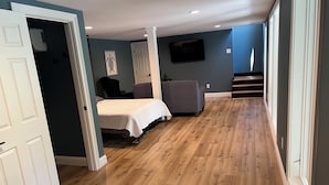 A bedroom with a bed, a chair, a TV, and a staircase leading to another room. - Incredible KY Lake Waterfront Home with Dock (Gilbertsville)
